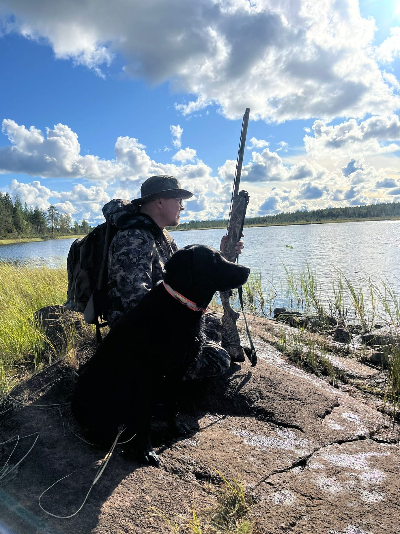 Metsästäjä ja koira kalliolla järven rannalla